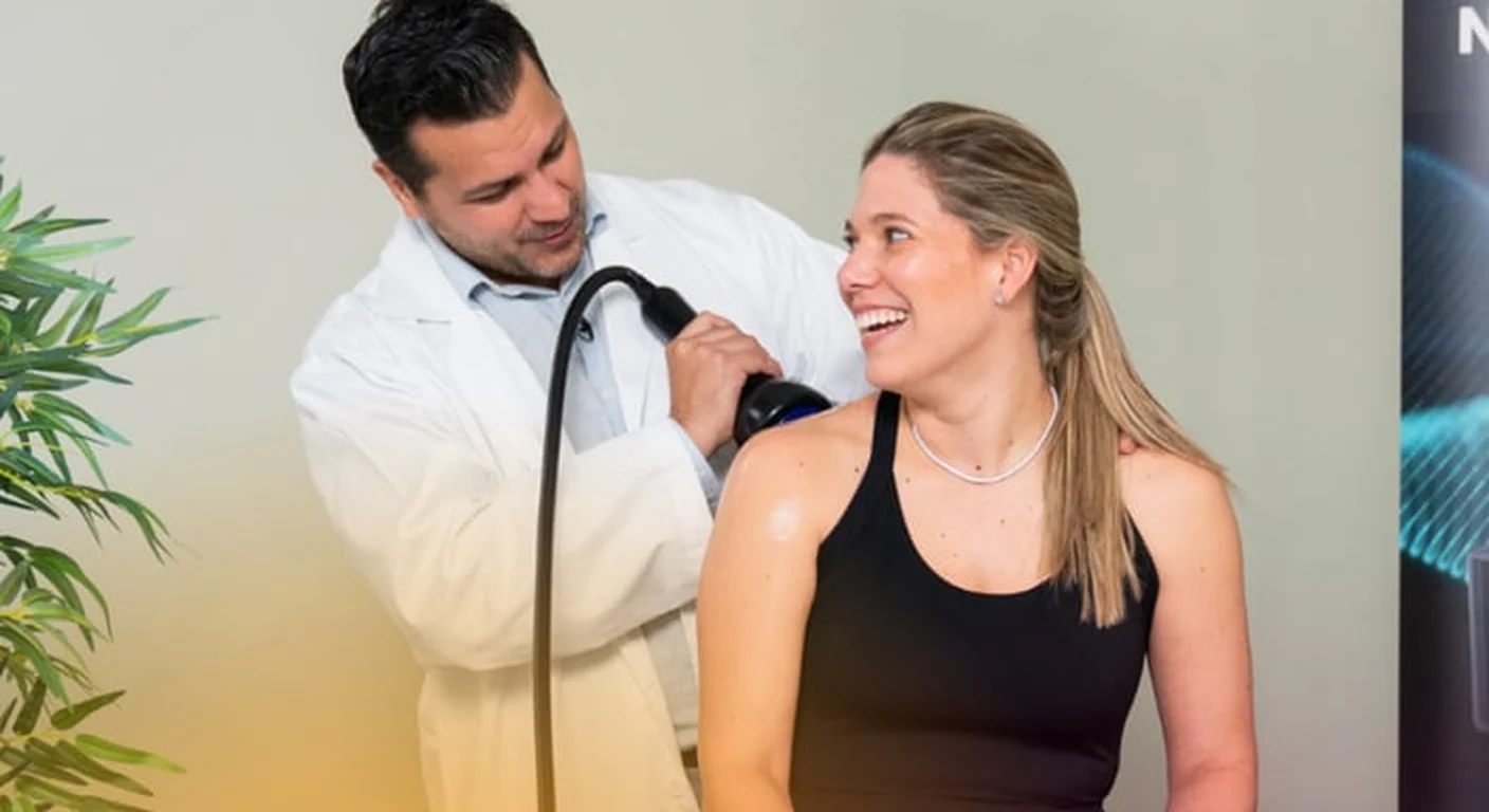 A clinician applies the shockwave applicator to a seated patient's shoulder during an in-office session.
